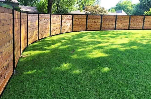 Curved wooden fence with metal posts surrounding a lush green lawn in a residential backyard.